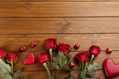 Photo of Flat lay composition with beautiful red roses and heart shaped candies on wooden background, space for text. Valentine's Day celebration