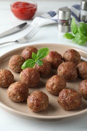 Tasty cooked meatballs with basil on white table