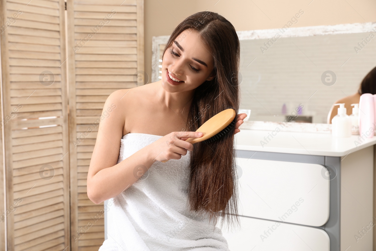 Photo of Beautiful smiling young woman with hair brush in bathroom