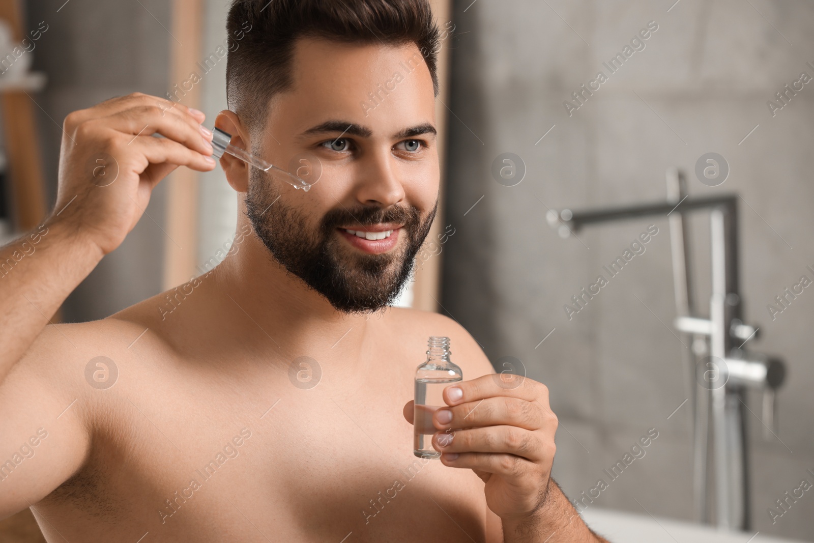 Photo of Handsome man applying cosmetic serum onto his face in bathroom