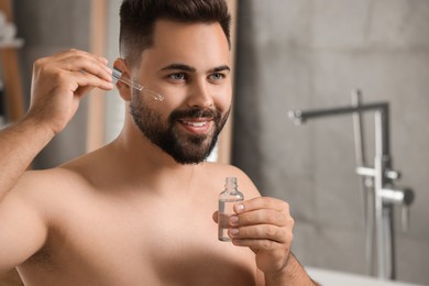 Handsome man applying cosmetic serum onto his face in bathroom