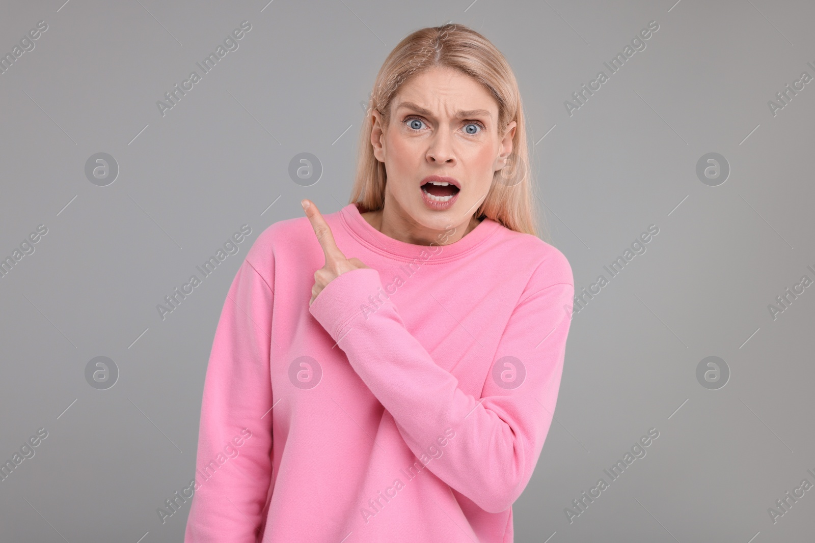 Photo of Surprised woman pointing at something on grey background