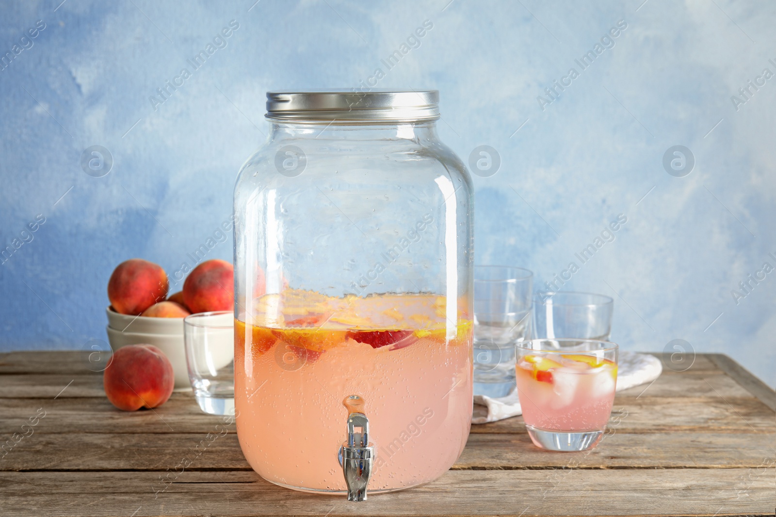 Photo of Peach cocktail in glass and jar with tap on table. Refreshing drink