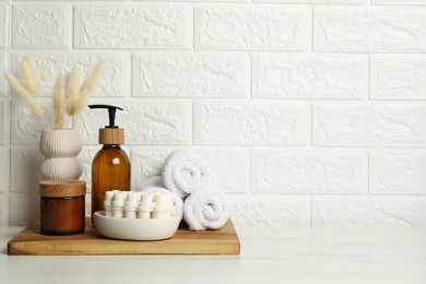 Photo of Different bath accessories, personal care products and spikelets in vase on white table near brick wall, space for text