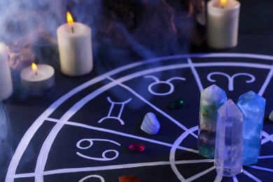 Natural stones for zodiac signs, drawn astrology chart and burning candles on black table