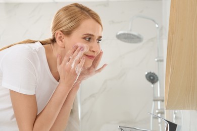 Happy young woman washing face in bathroom