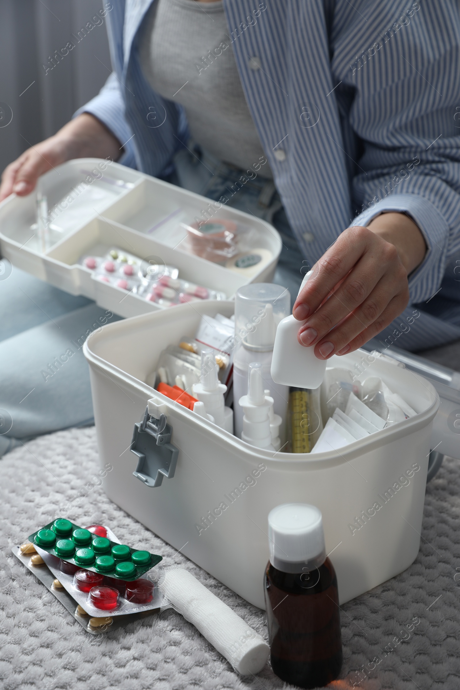 Photo of Woman putting medicament into first aid kit indoors, closeup