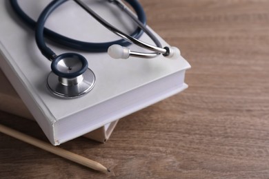 Photo of Student textbooks, pencil and stethoscope on wooden table, closeup. Medical education