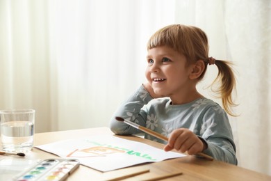 Photo of Cute little girl drawing at wooden table indoors. Child`s art