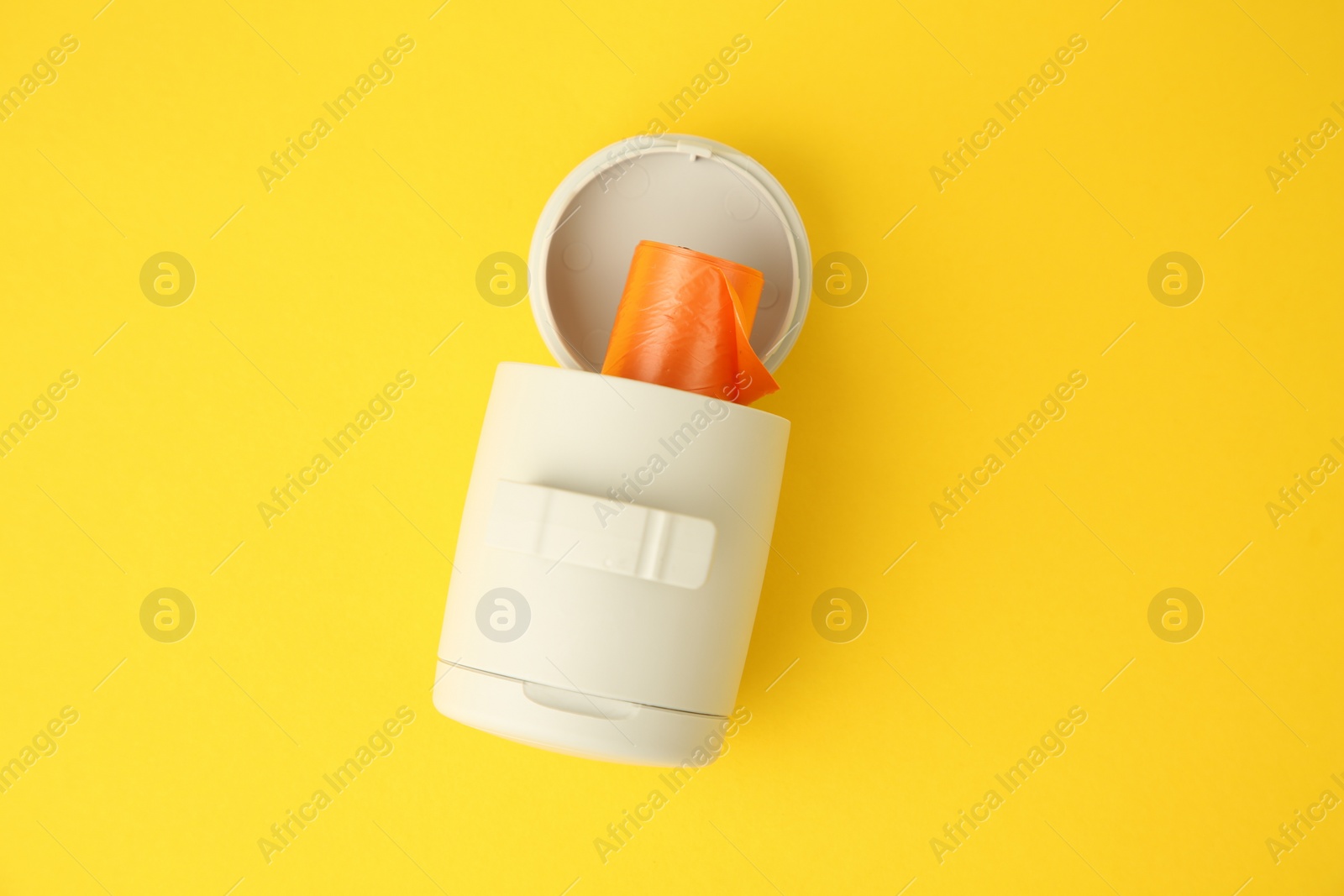 Photo of Dispenser with dog waste bags on yellow background, top view