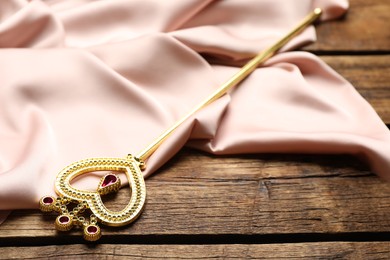 Photo of Beautiful golden magic wand and pink fabric on wooden table
