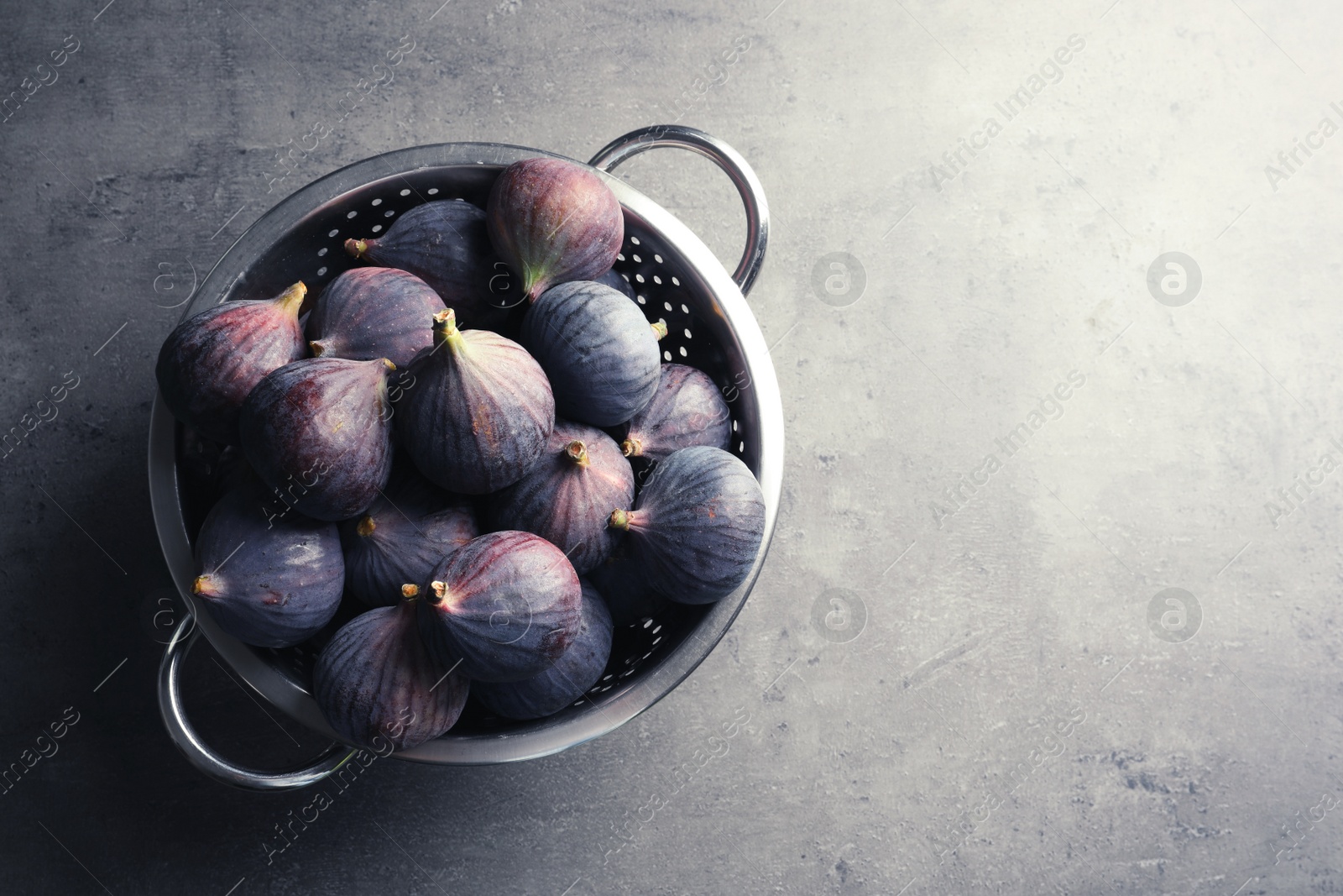 Photo of Colander with fresh ripe figs on gray background, top view. Space for text