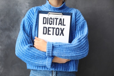 Photo of Woman holding clipboard with phrase DIGITAL DETOX on grey background, closeup