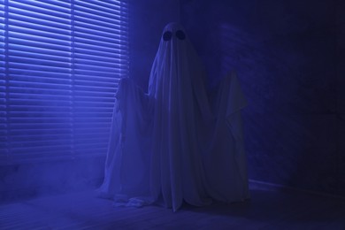 Creepy ghost. Woman covered with sheet near window in blue light