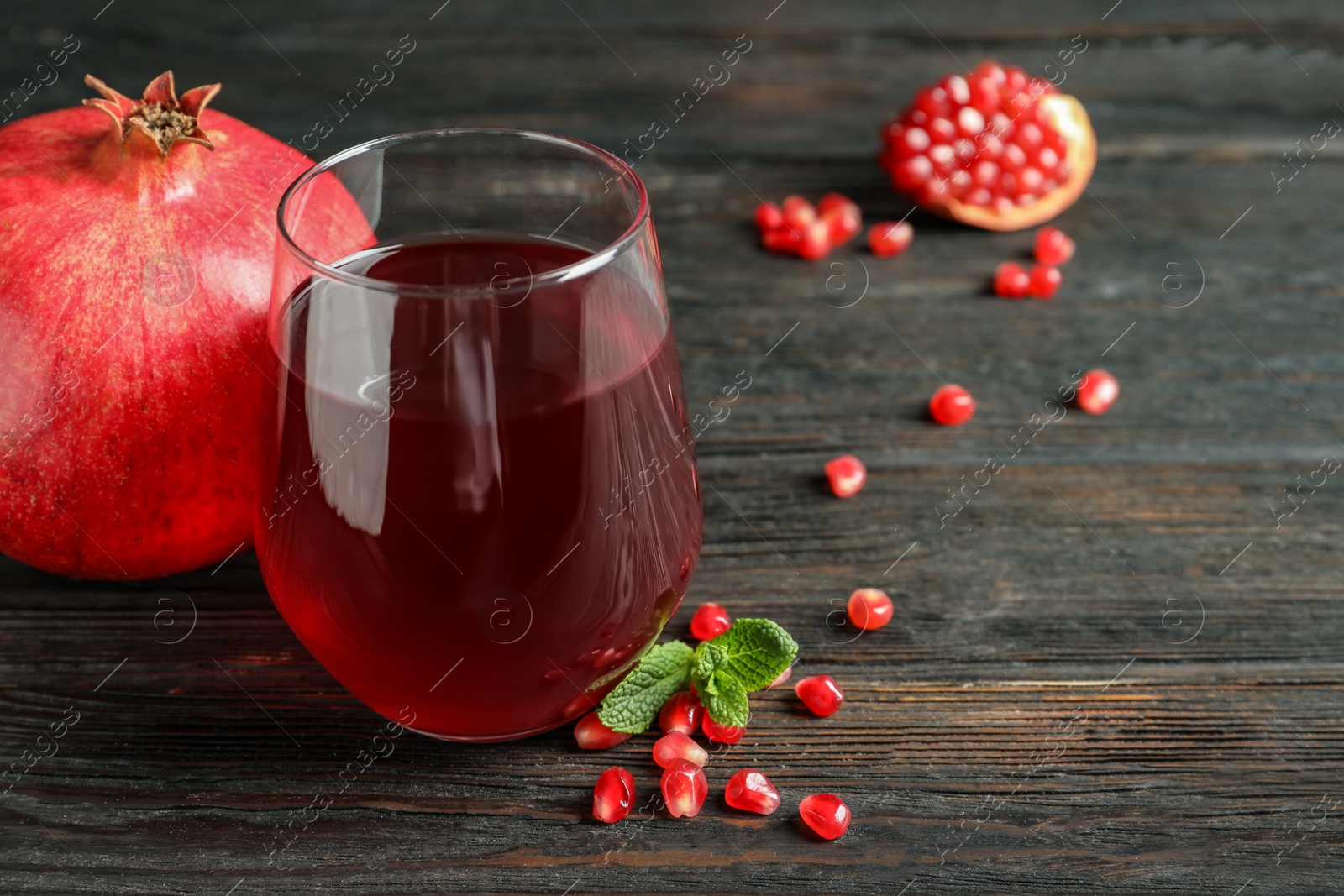 Photo of Glass of pomegranate juice and fresh fruits on wooden background, space for text