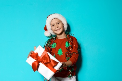 Photo of Cute little boy in handmade Christmas sweater and hat with gift on color background