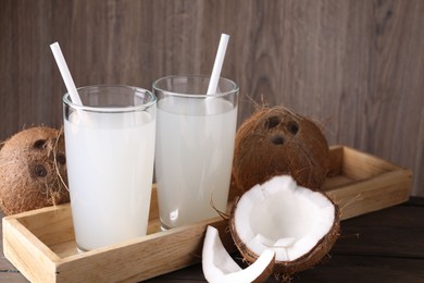 Glasses of coconut water with straws and nuts on wooden table