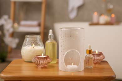 Photo of Aroma lamp, bottles of oils and candles on wooden table in bathroom