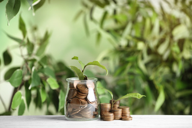 Coins and green sprout on white wooden table against blurred background. Money savings