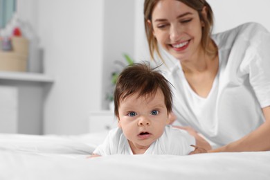 Cute little baby and mother on cosy bed in room, space for text