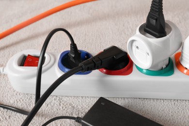 Photo of Power strip with different electrical plugs on white carpet, closeup