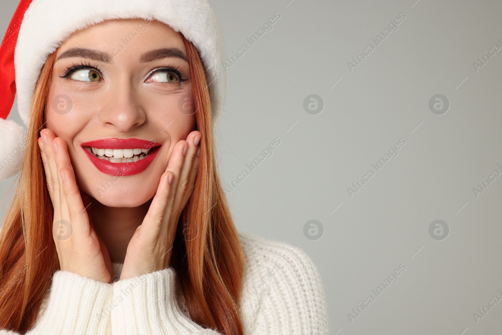 Photo of Young woman in Santa hat on light grey background, space for text. Christmas celebration