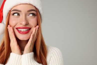 Young woman in Santa hat on light grey background, space for text. Christmas celebration