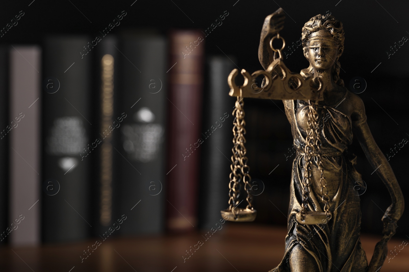 Photo of Symbol of fair treatment under law. Statue of Lady Justice near books on table, closeup with space for text