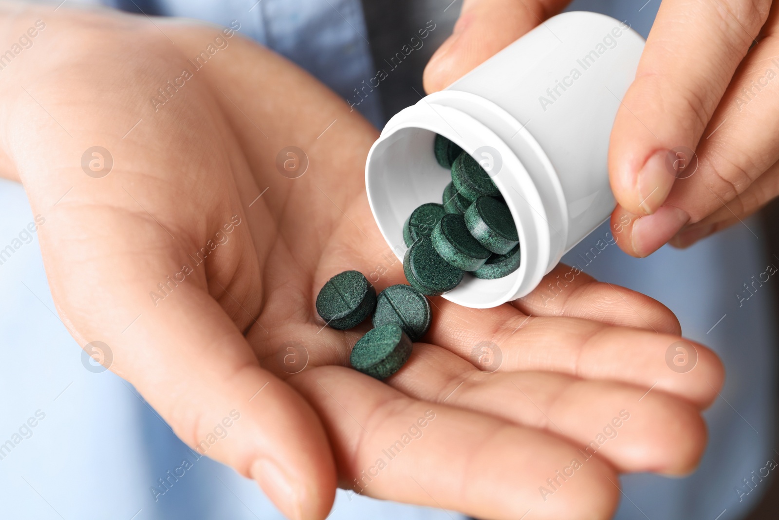 Photo of Woman pouring spirulina pills from bottle into hand, closeup