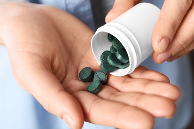 Photo of Woman pouring spirulina pills from bottle into hand, closeup