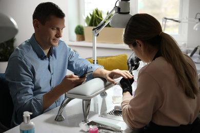 Professional manicurist working with client in beauty salon