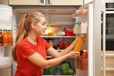 Photo of Young woman with juice near refrigerator at home