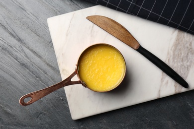 Photo of Stone board with saucepan of clarified butter and knife on table, flat lay