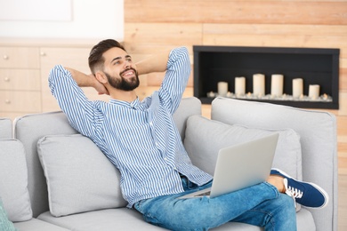 Relaxed handsome young man with laptop on sofa at home. Taking break during work