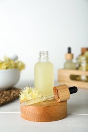 Bottle of essential oil and linden flowers on white wooden table