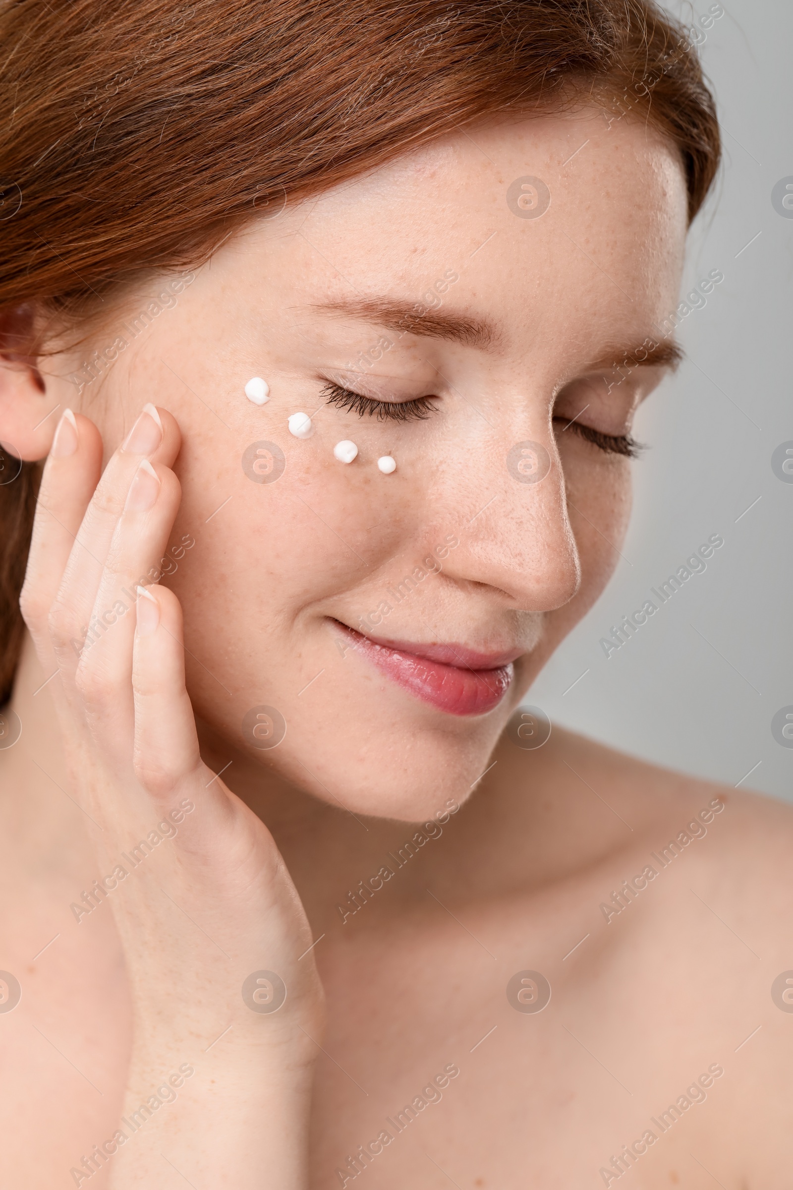 Photo of Beautiful woman with freckles and cream on her face against grey background, closeup