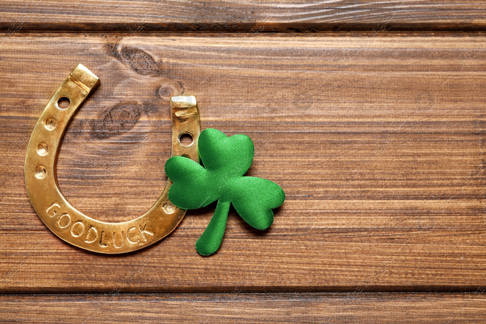 Photo of Clover leaf and horseshoe on wooden table, flat lay with space for text. St. Patrick's Day celebration