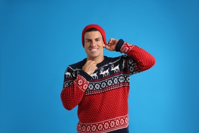 Photo of Handsome man in Christmas sweater and hat on blue background