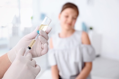 Doctor filling syringe with medicine and child on background. Vaccination day