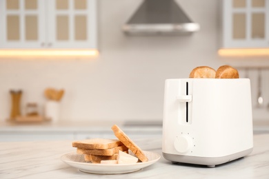 Photo of Modern toaster and bread slices on white marble table in kitchen