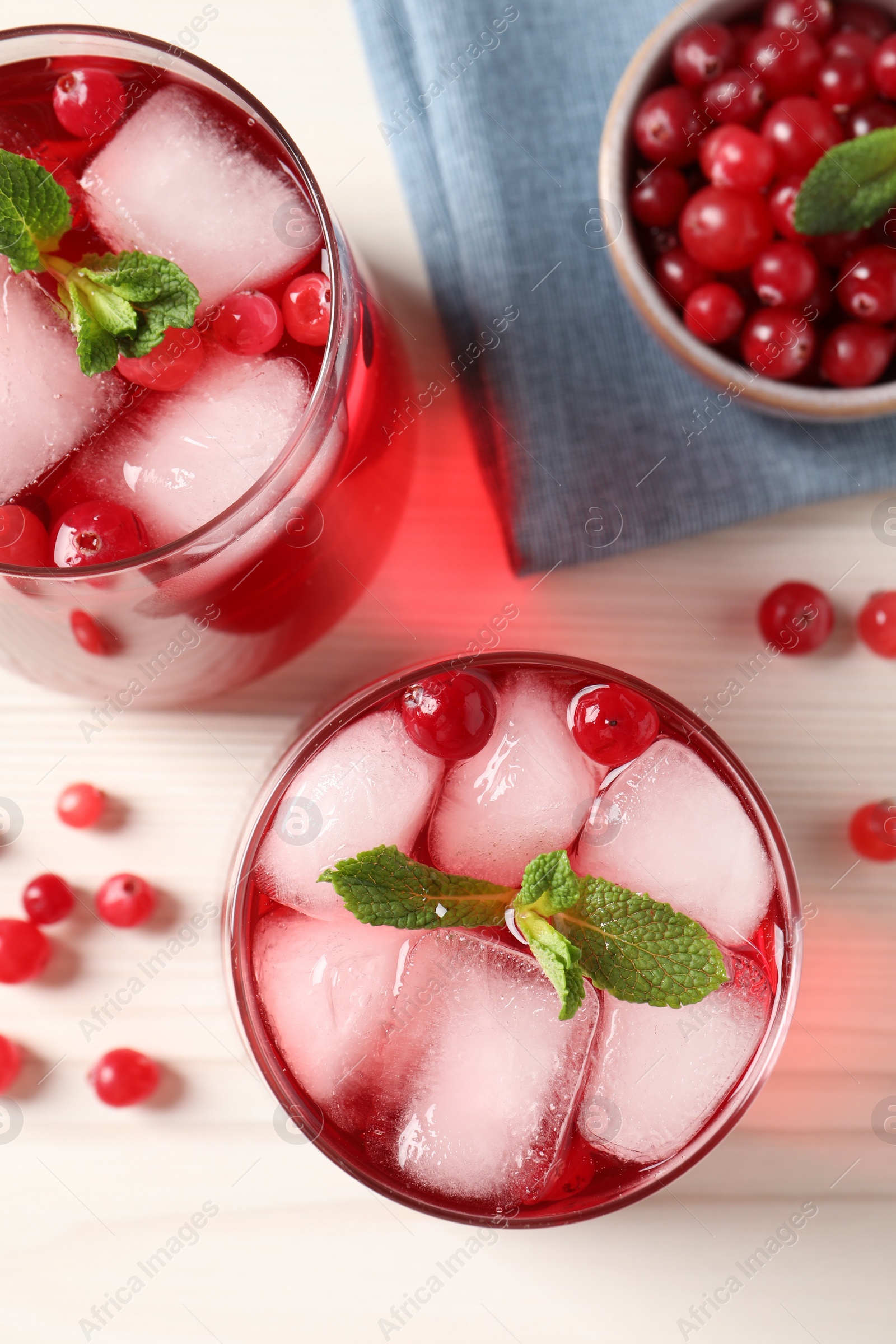 Photo of Tasty cranberry juice with ice cubes in glasses and fresh berries on white wooden table, flat lay