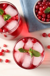 Photo of Tasty cranberry juice with ice cubes in glasses and fresh berries on white wooden table, flat lay