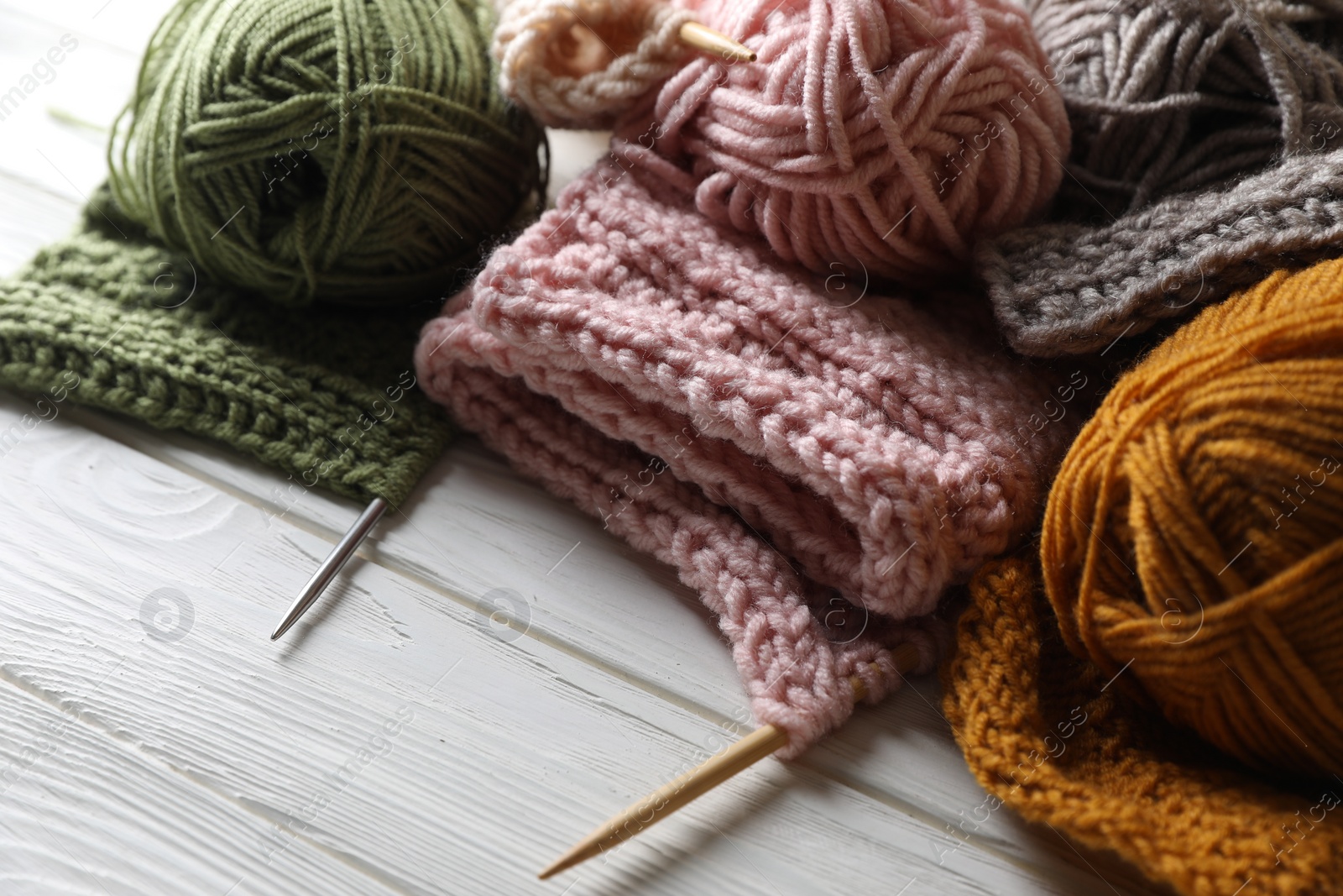 Photo of Balls of soft yarns, knitting and needles on white wooden table