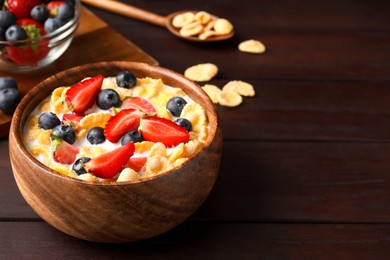 Photo of Bowl of tasty crispy corn flakes with milk and berries on wooden table. Space for text
