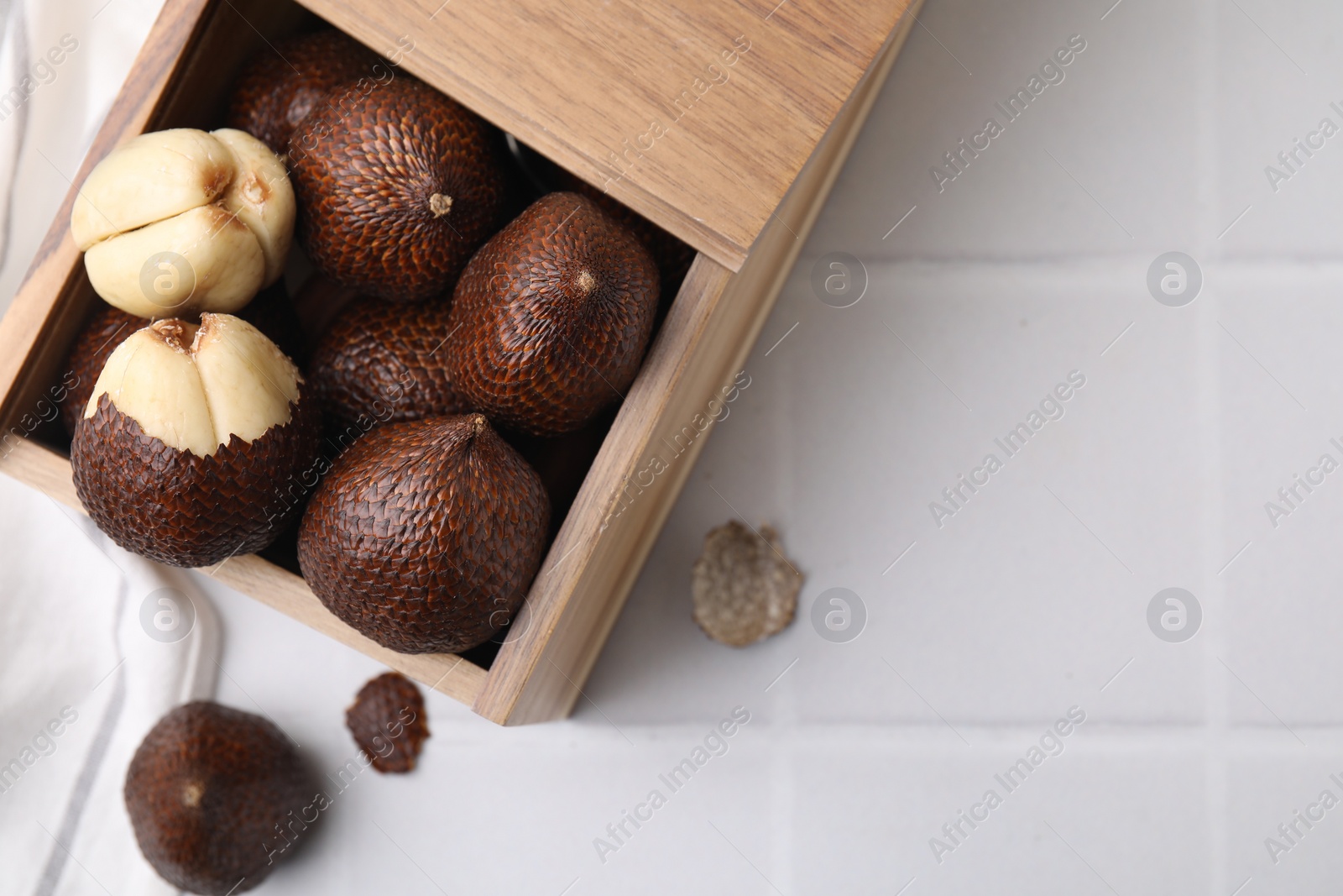 Photo of Wooden crate with fresh salak fruits on white tiled table, top view. Space for text