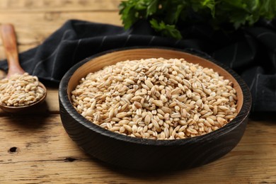 Photo of Dry pearl barley in bowl and spoon on wooden table, closeup