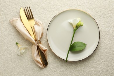 Photo of Stylish setting with cutlery, napkin, flowers and plate on light textured table, flat lay