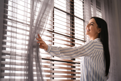 Photo of Woman opening window curtain at home in morning