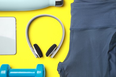 Photo of Stylish sports leggings, dumbbell, thermo bottle, headphones and smartphone on yellow background, flat lay