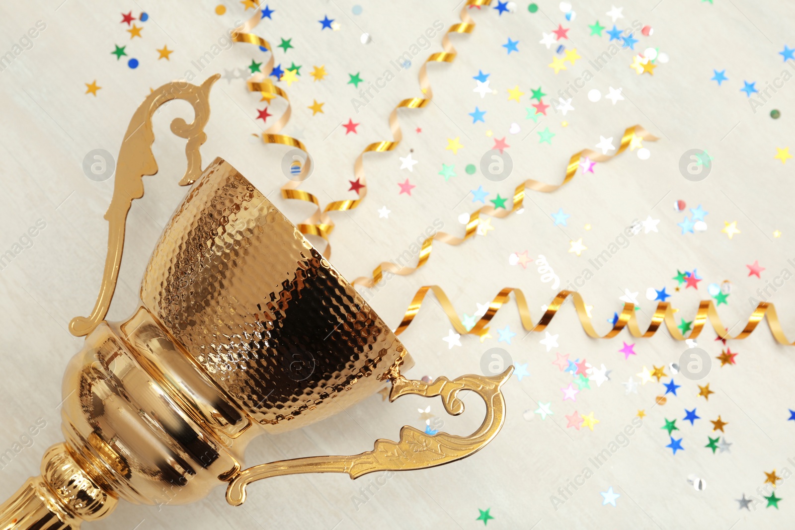 Photo of Golden trophy cup with streamers on wooden background. Space for text